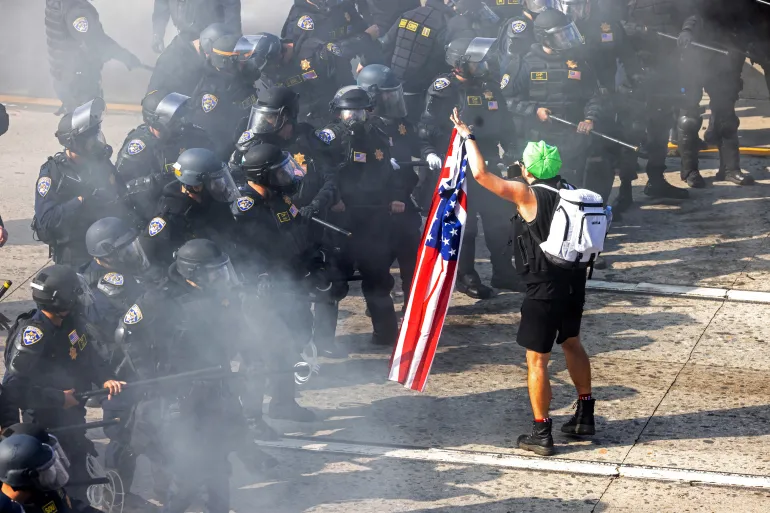 A demonstrator holds a US flag opposite California Highway Patrol officers